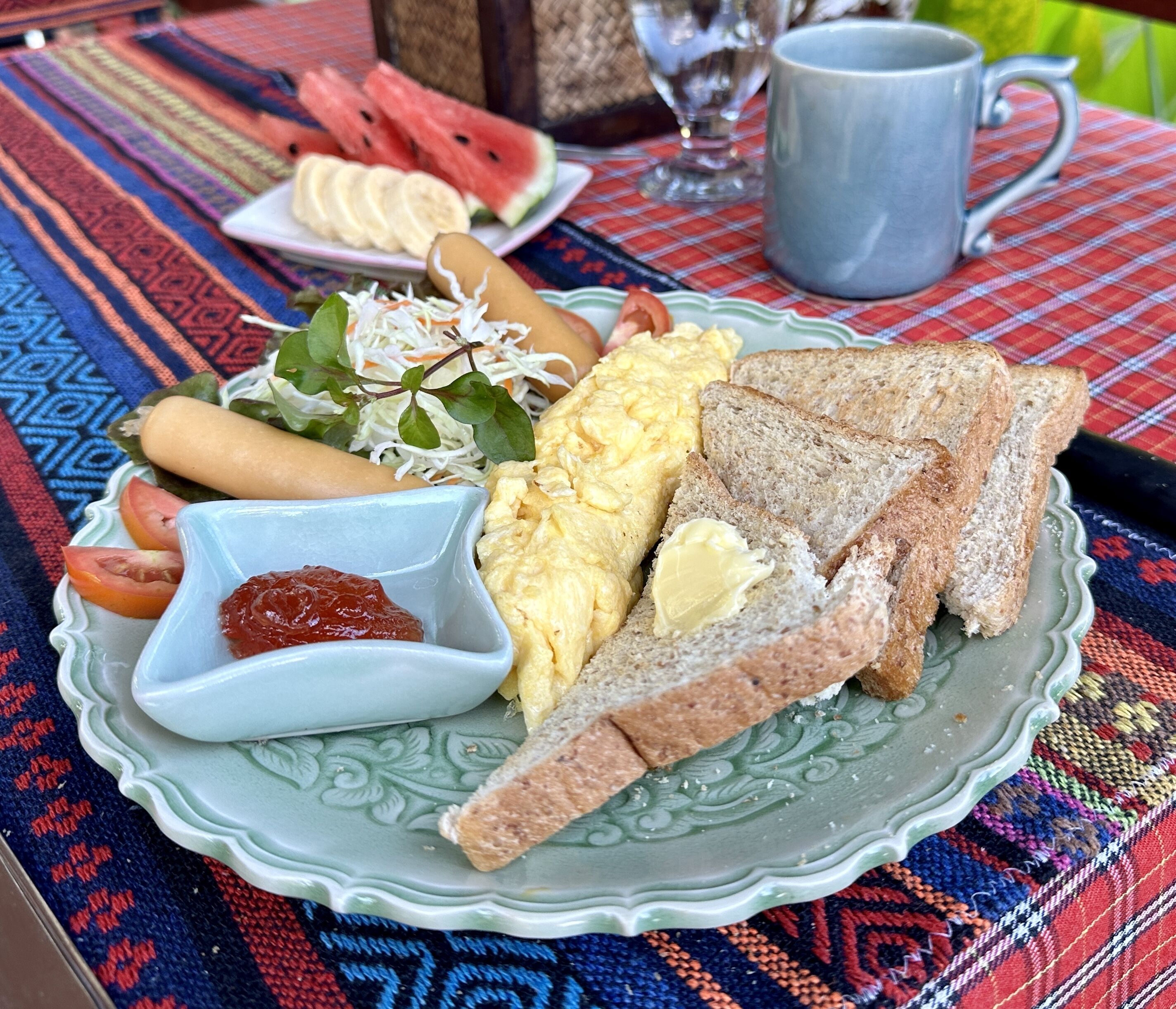 A plate with scrambled eggs, toast, tomatoes, and a small bowl of jam.
