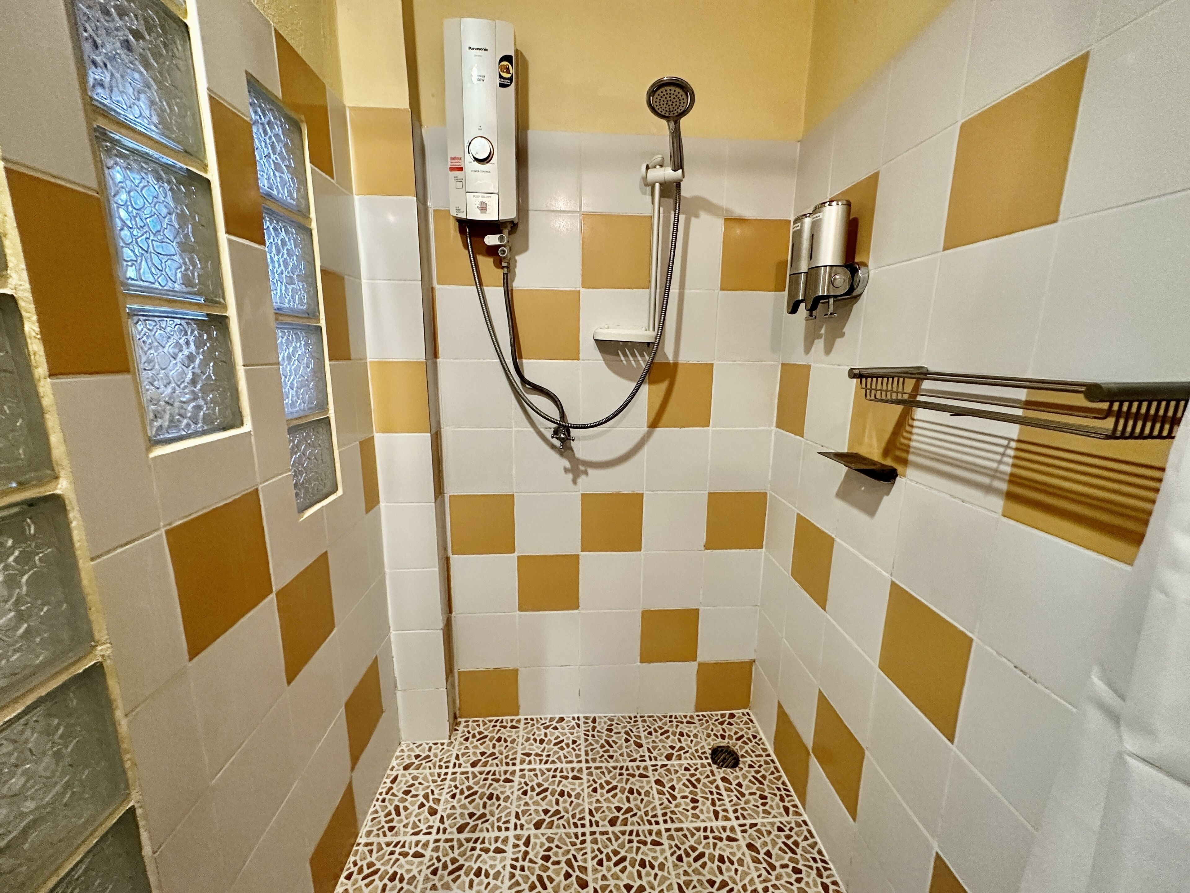 Une salle de bain avec un carrelage à motifs à carreaux, une douche équipée d’un pommeau de douche amovible et un porte-serviettes.