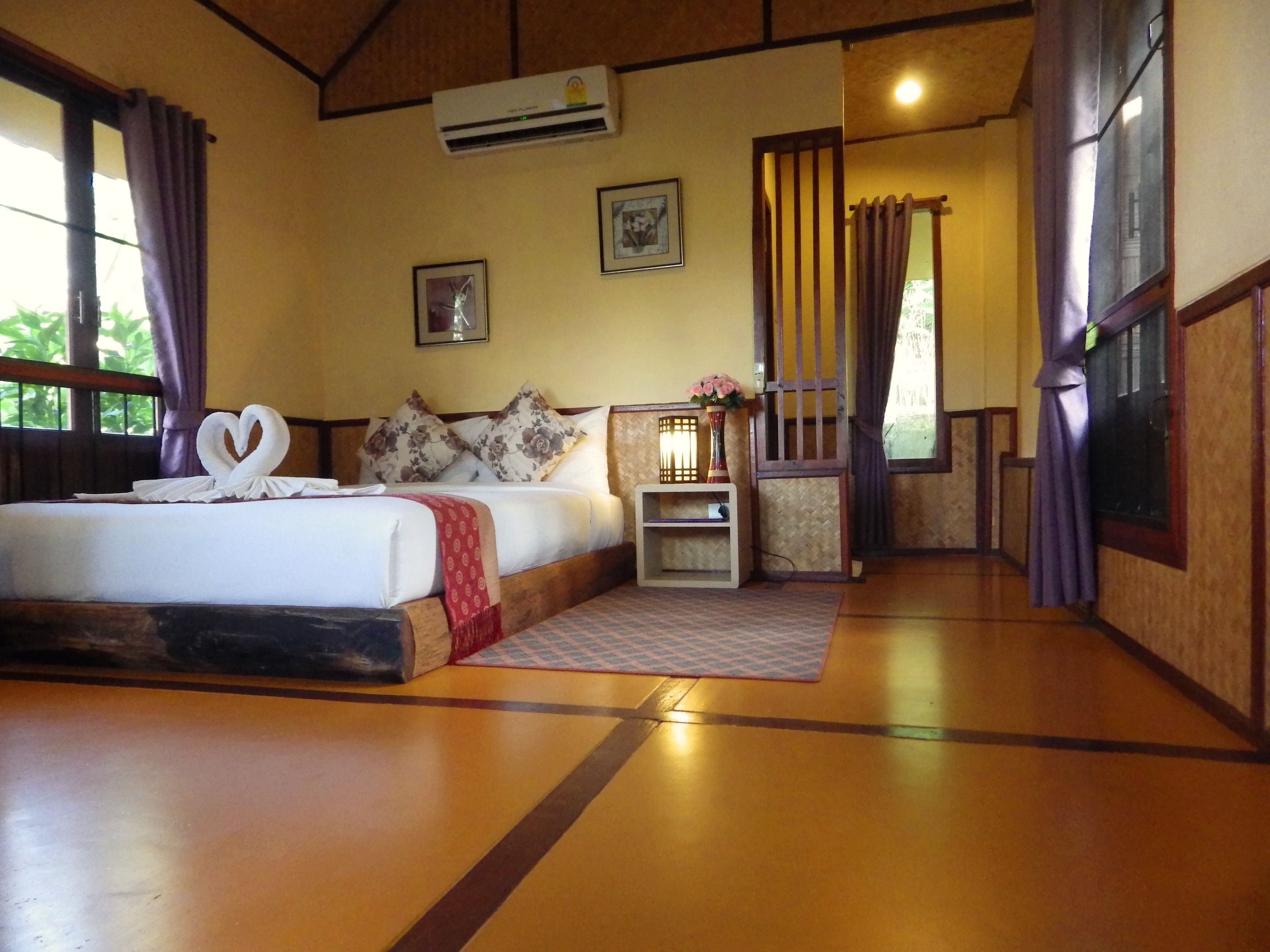 A hotel room with a bed, a bedside table with a lamp, and a window with curtains.