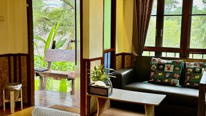 A cozy room with a sofa, a small table, and a view of greenery outside. - PuraVida Pai Resort (Pai)