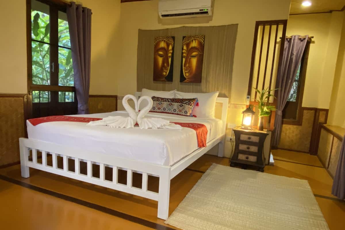 Habitación de hotel con cama, mesita de noche, lámpara, ventana con cortinas y aire acondicionado instalado en la pared.