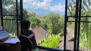 A room with a large window offering a view of a mountainous landscape, a desk with a laptop, and a chair. - PuraVida Pai Resort (Pai)