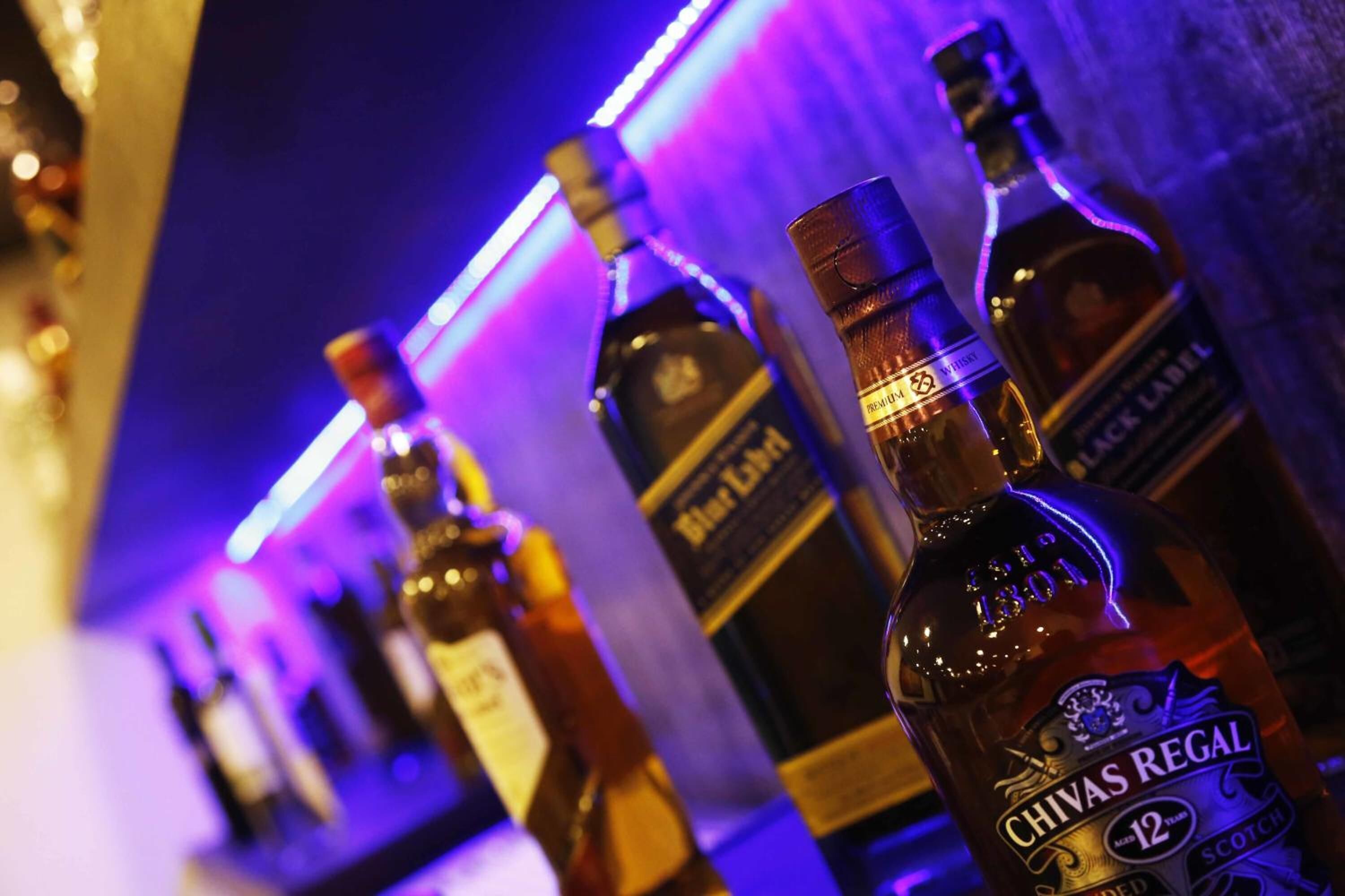 A row of whisky bottles on a bar counter with a blue neon light in the background.