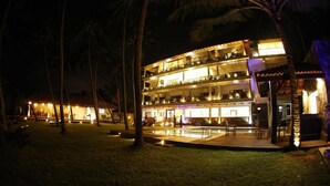 A multi-story hotel with outdoor seating and a pool area, surrounded by palm trees. - Blue Beach (Wadduwa)
