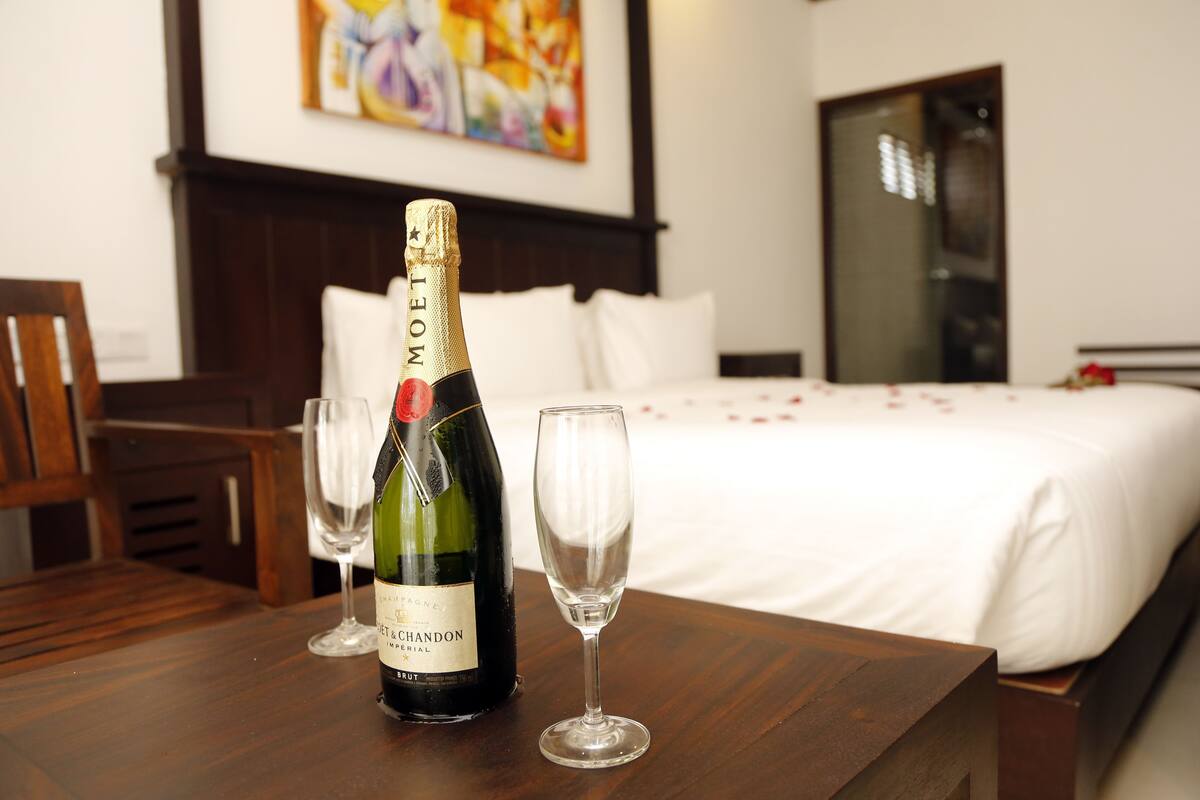 A bottle of Moët & Chandon champagne and two glasses on a wooden table in a hotel room with a bed and a painting in the background.