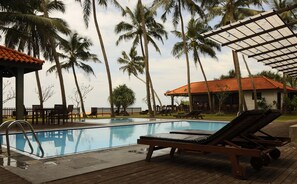 A pool area with lounge chairs, a wooden deck, and palm trees.