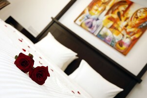 Una cama bien hecha con sábanas blancas y dos rosas rojas. Un cuadro se ve en la pared detrás de la cama.