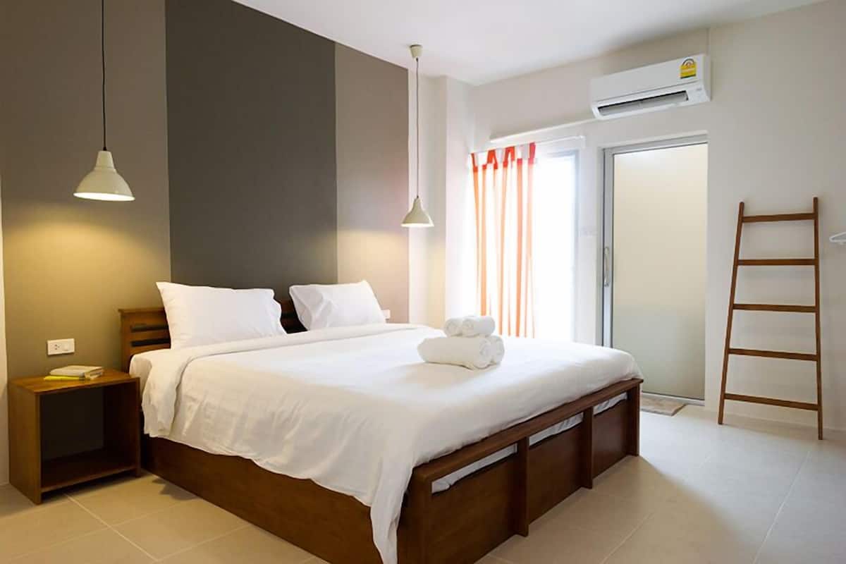 A bedroom with a bed, bedside tables, a ladder, and a window with curtains.