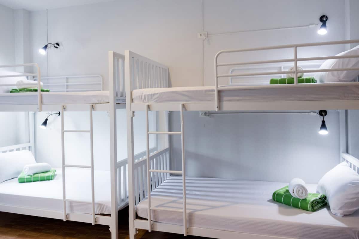 A dormitory room with bunk beds, each with a small bedside table and lamp.