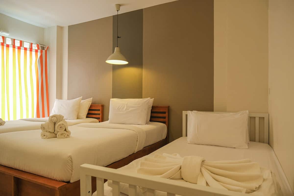 A hotel room with two beds, a hanging light fixture, and a window with striped curtains.
