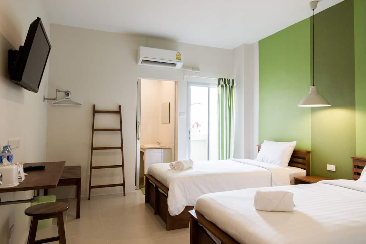 A hotel room with two beds, a desk with a chair, a TV mounted on the wall, and an air conditioning unit.
