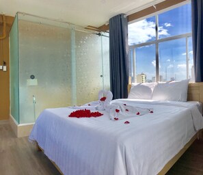 A hotel room with a bed, a glass shower enclosure, and a view of the city skyline through large windows. - 99 Bui Vien Hotel (Ho Chi Minh City)