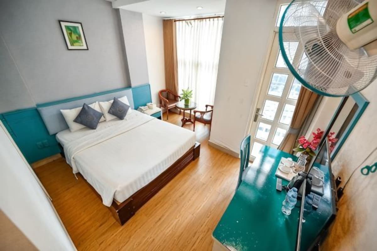 Habitación de hotel con cama, escritorio, silla, ventilador y ventana.