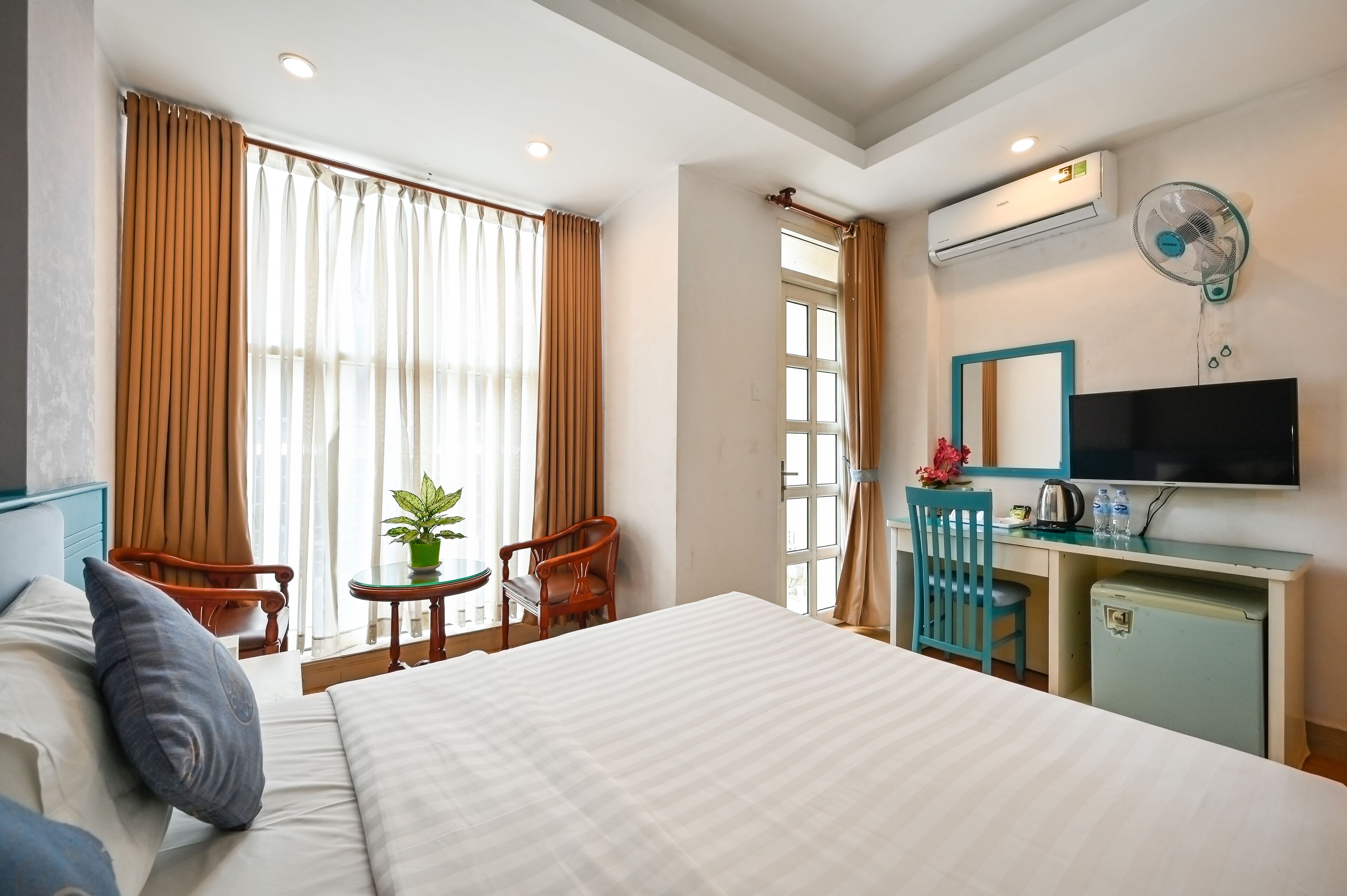 A hotel room with a large bed, a desk with a TV, a small fridge, and a window with curtains.