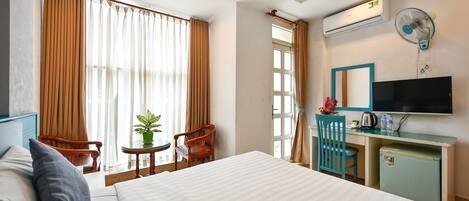 A hotel room with a large bed, a desk with a TV, a small fridge, and a window with curtains.