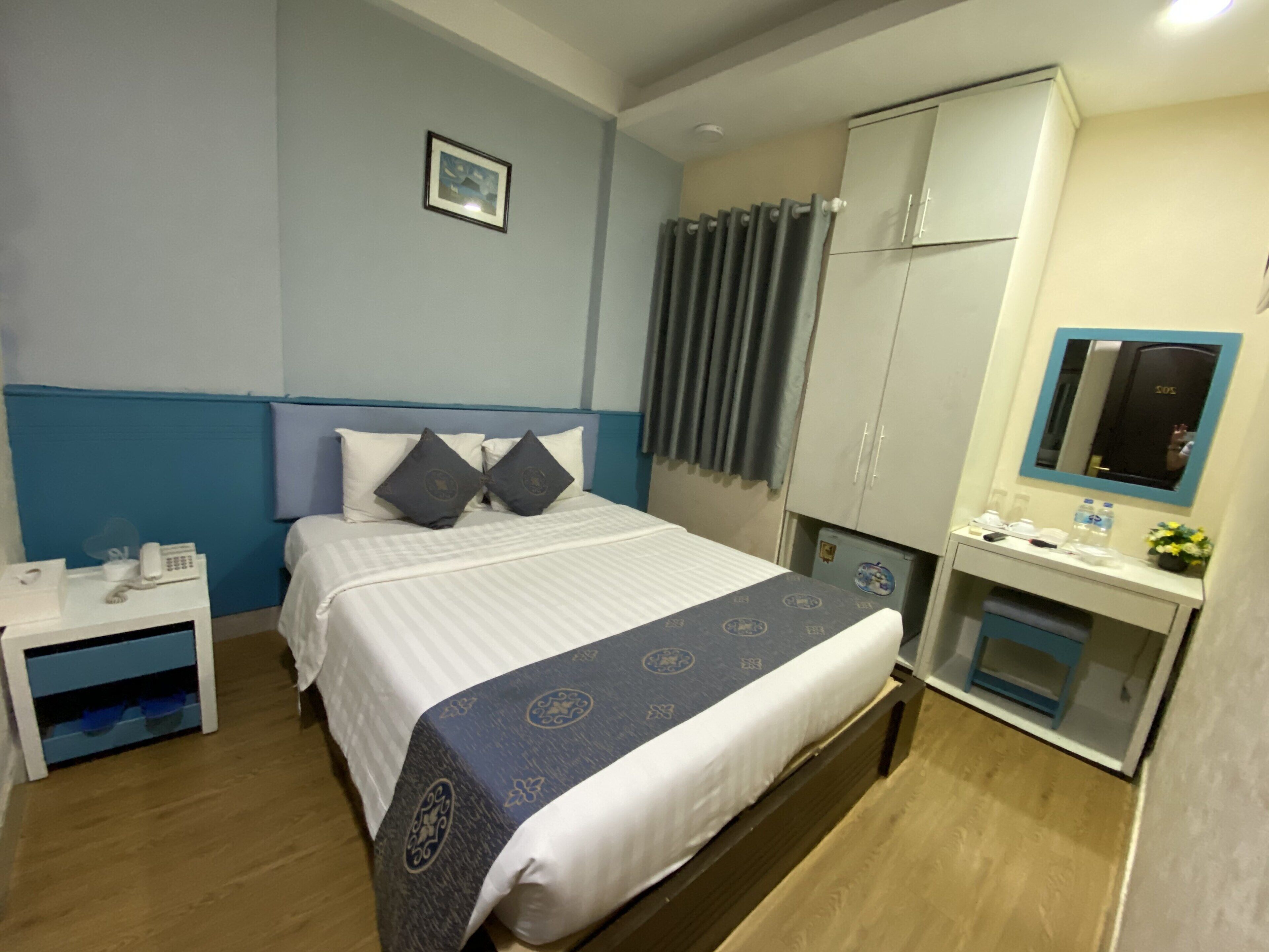 Una habitación de hotel con cama, mesita de noche, armario y un pequeño escritorio con espejo.