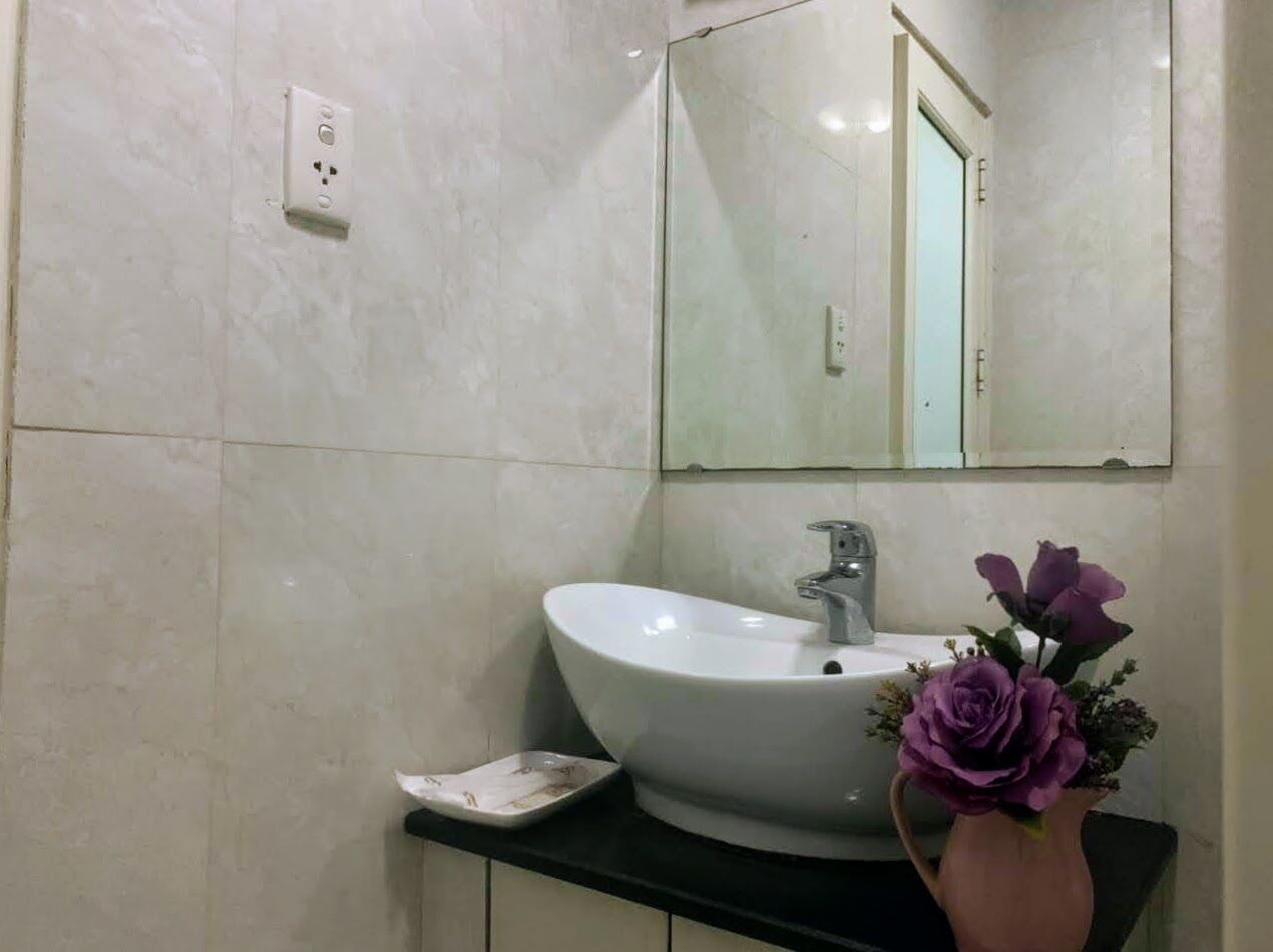 Een badkamer met een witte wastafel, een spiegel en een vaas met paarse bloemen.