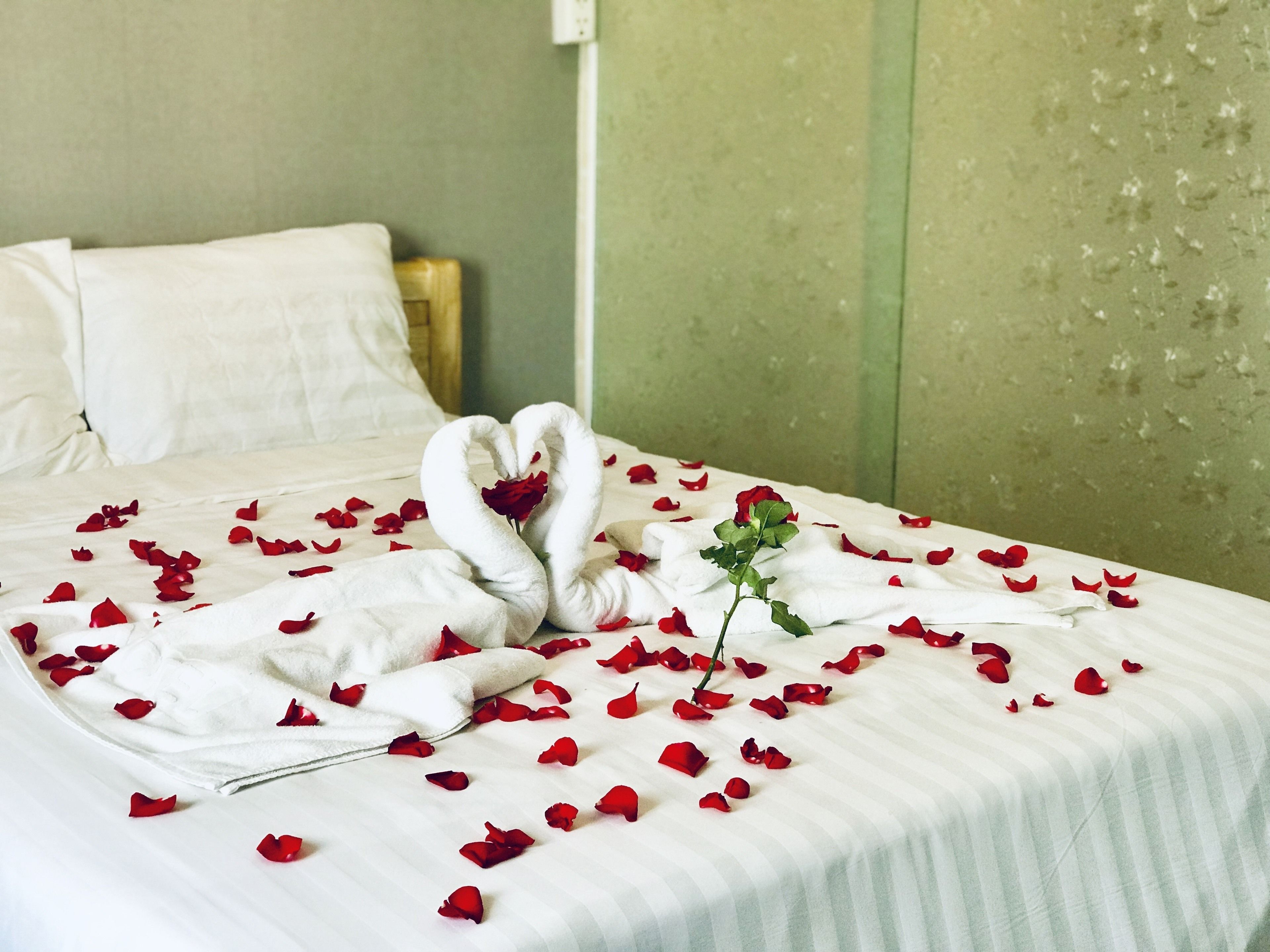 Una cama con pétalos de rosa y una rosa, y dos toallas dispuestas en forma de corazón.
