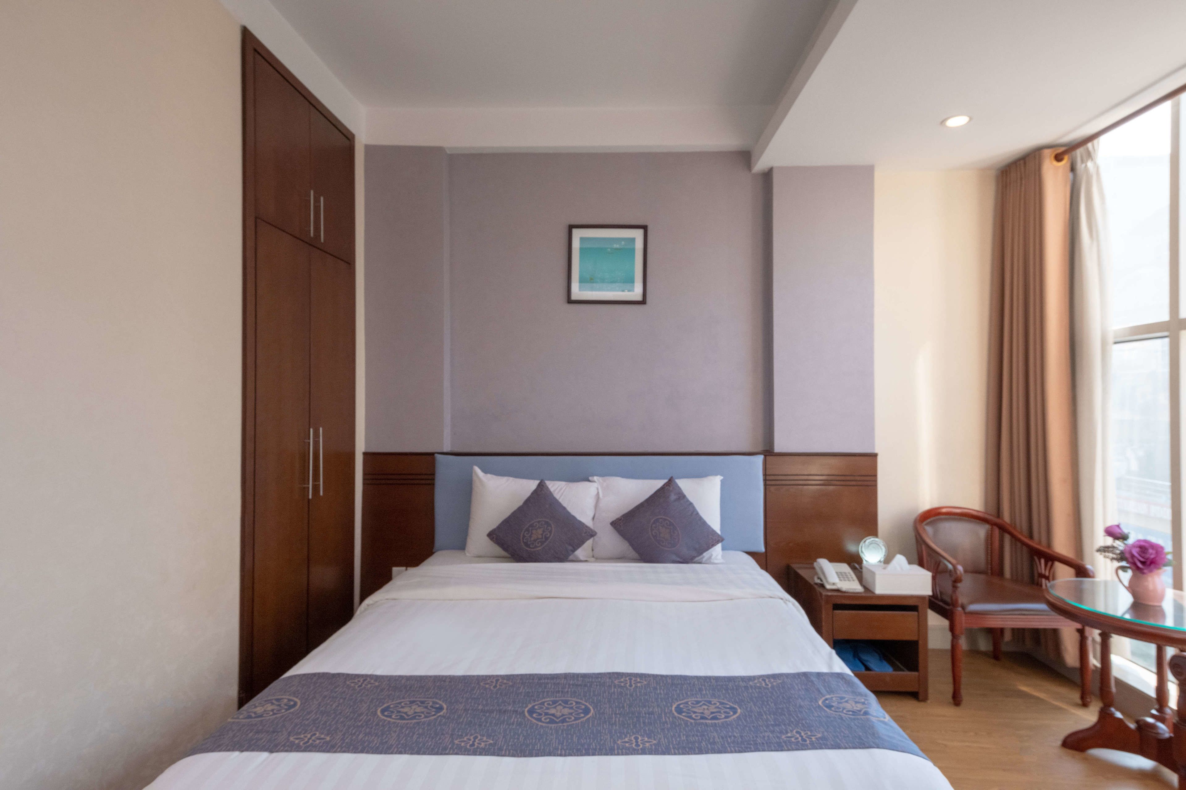 Une chambre d’hôtel avec un lit, une table de chevet, une chaise, une table et une fenêtre avec des rideaux.
