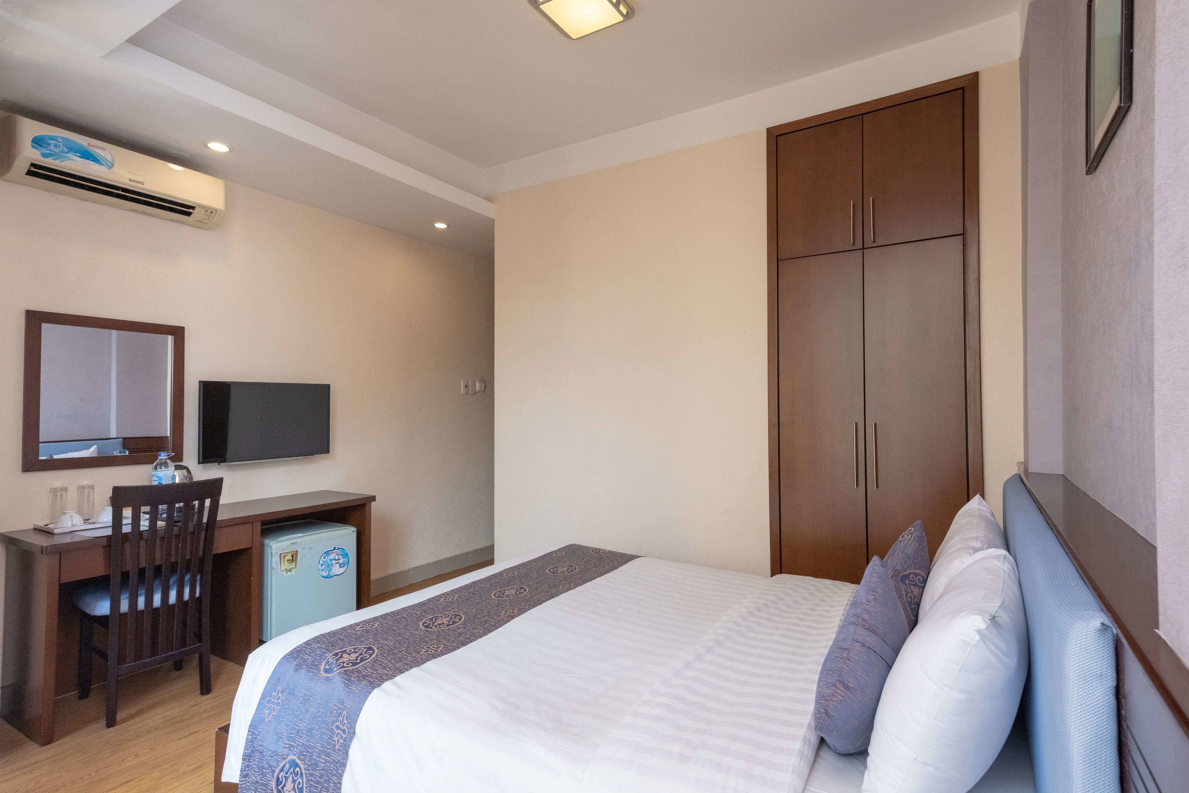 A hotel room with a bed, a desk with a chair, a television, and a wardrobe.