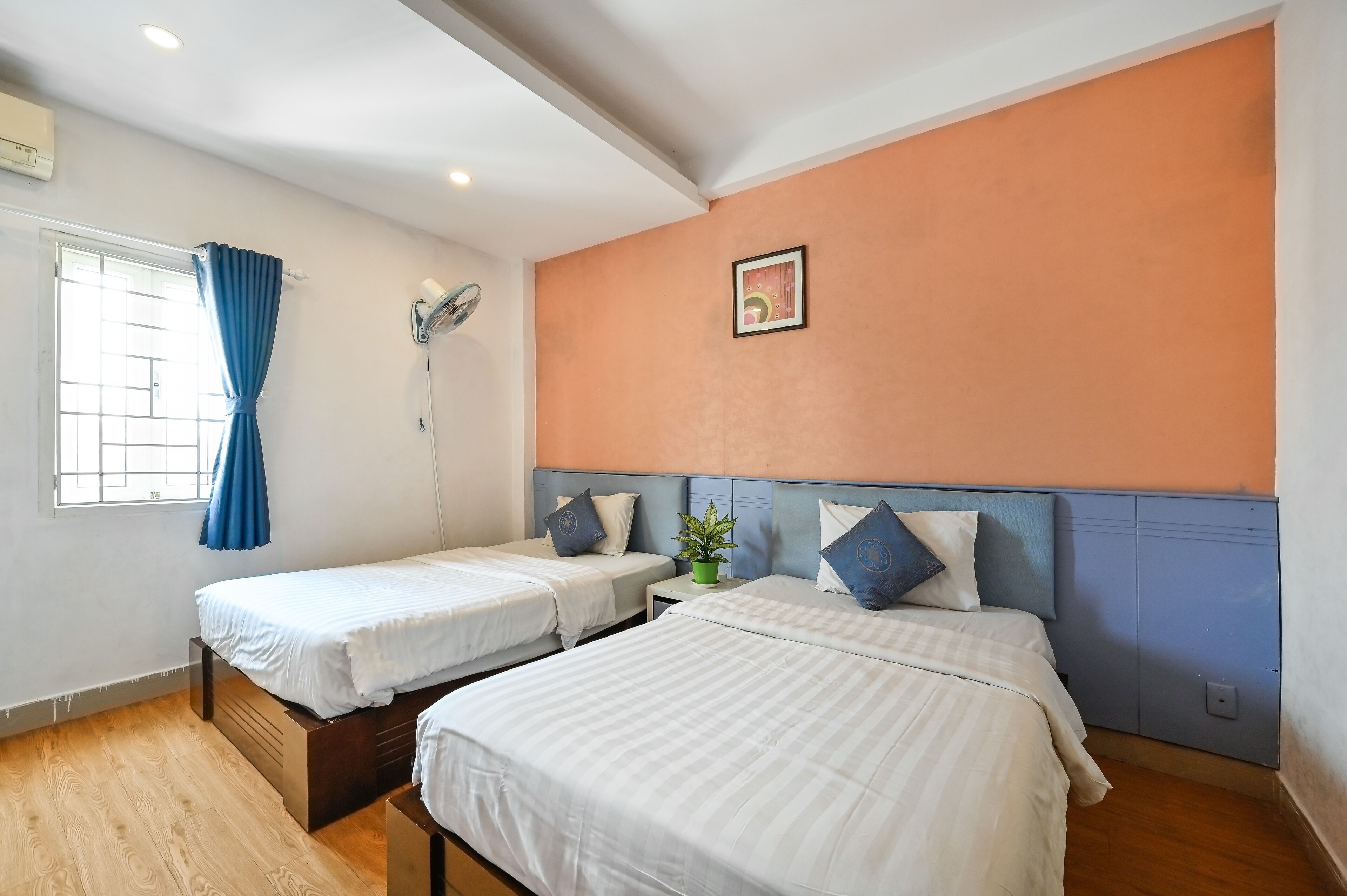 A hotel room with two single beds, a window with curtains, a ceiling fan, and a small potted plant.