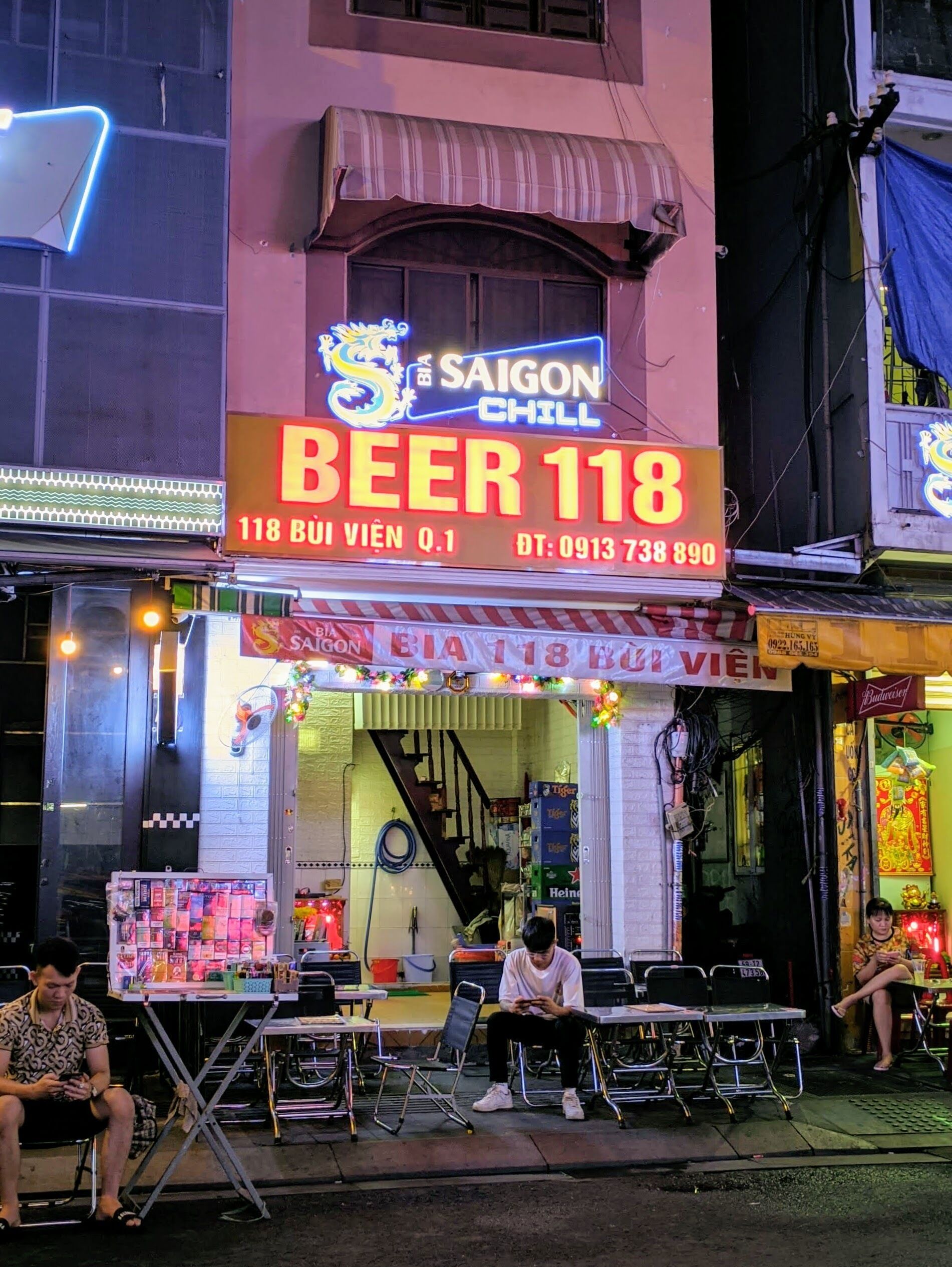 A building with a neon sign advertising "SAIGON BIA 118 BEER" and a staircase leading to the entrance.