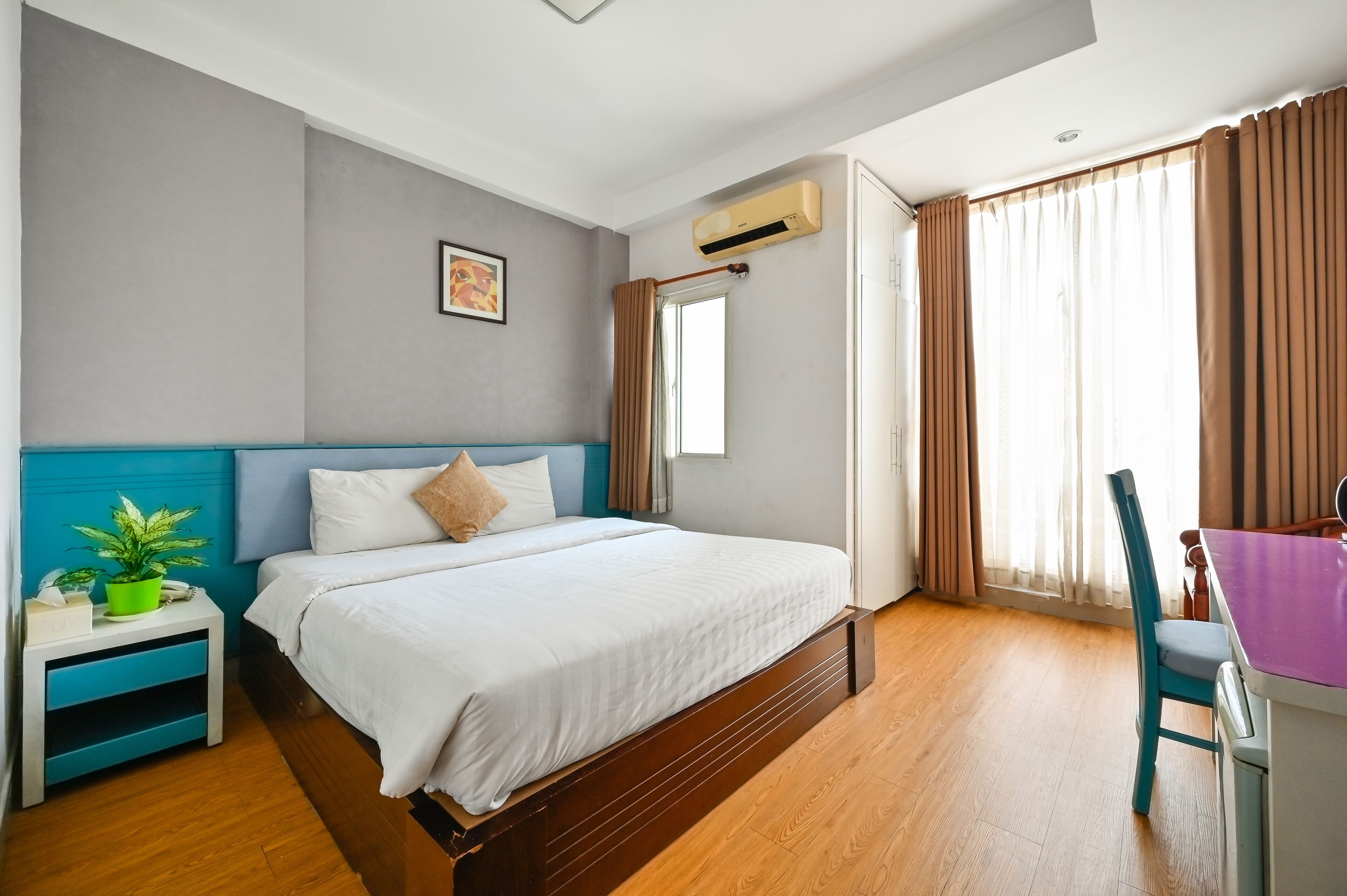 Une chambre d’hôtel avec un lit, une table de chevet, une chaise, un bureau et une fenêtre avec des rideaux.