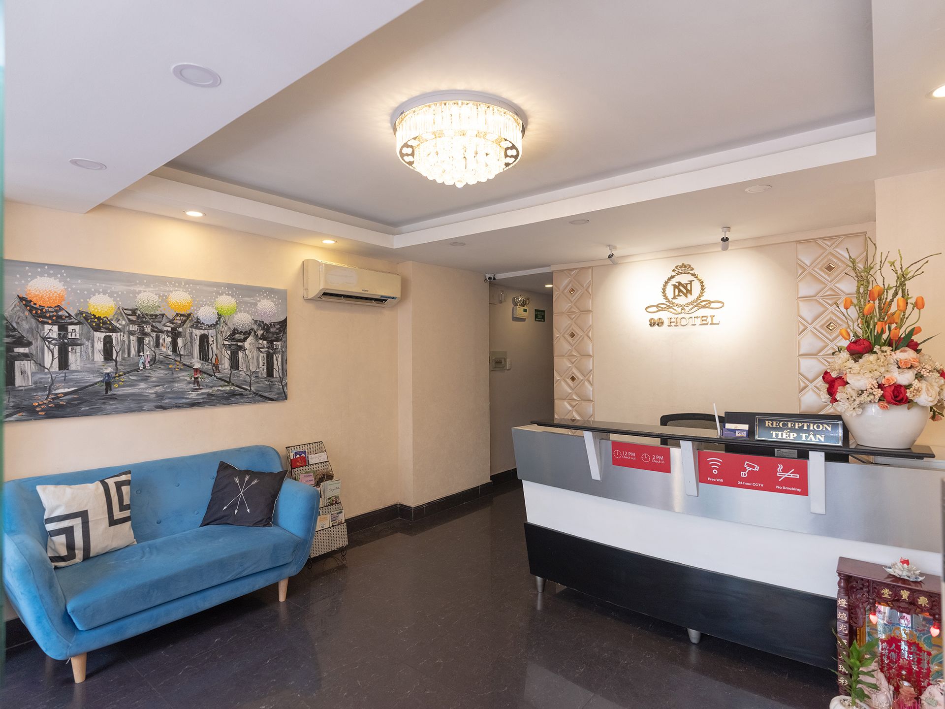 Ein Hotel-Empfangsbereich mit einer Rezeption, einer blauen Couch, einer Chandelüster und einem Gemälde an der Wand.