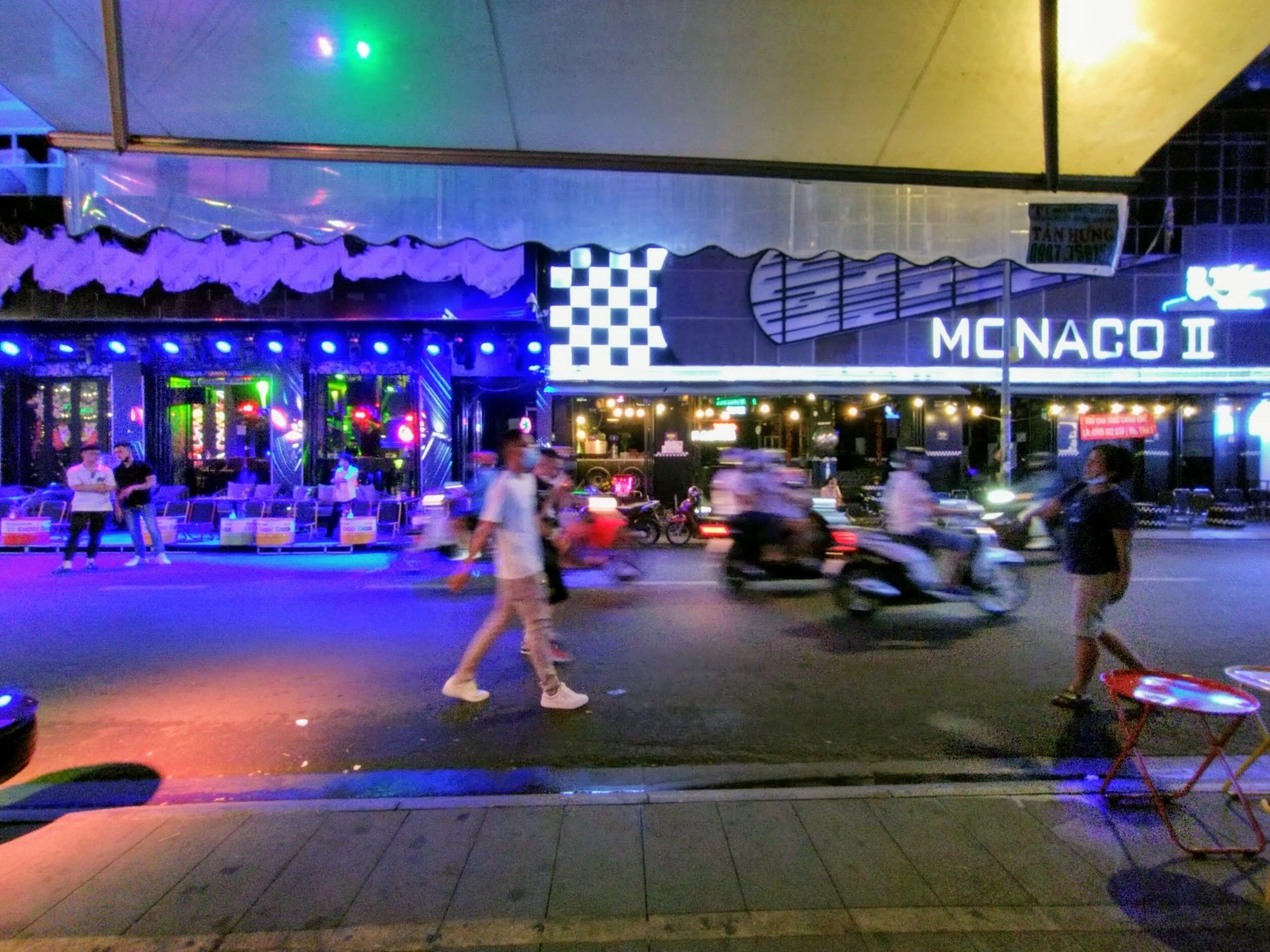 A street scene with a restaurant named "MCNACO II" and a neon sign.