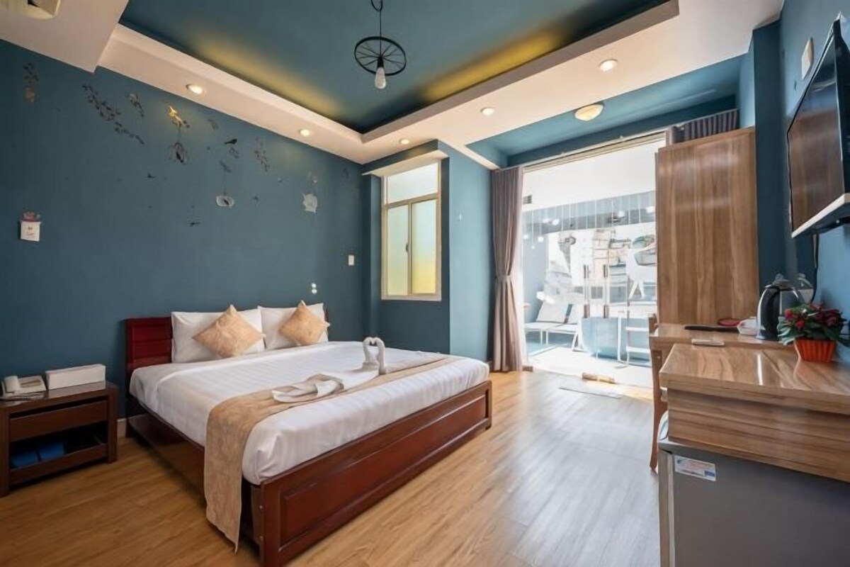 A hotel room with a bed, bedside table, and a view of the outside.