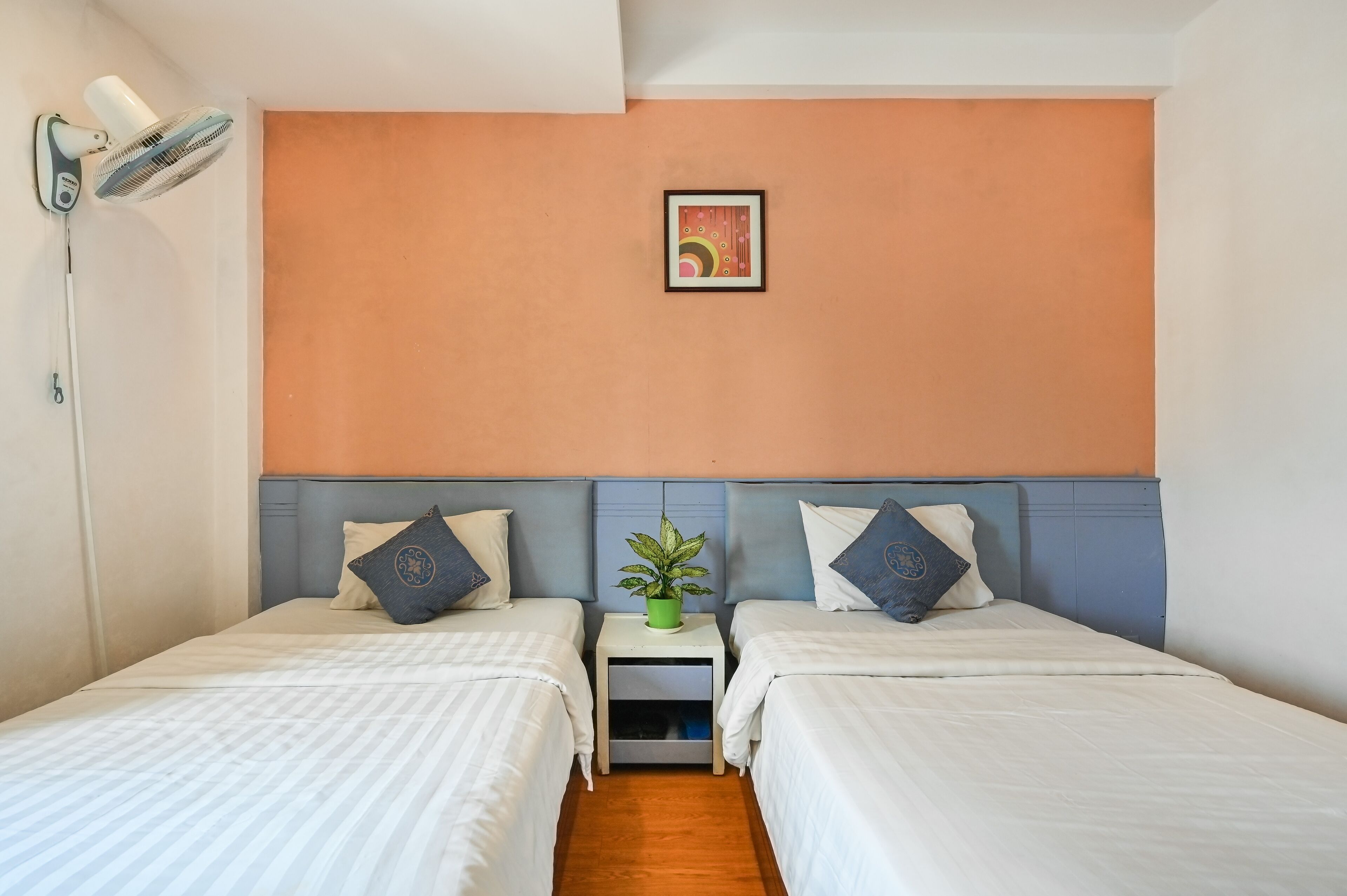 Una habitación de hotel con dos camas, una mesita de noche con una planta y un cuadro colgado en la pared.
