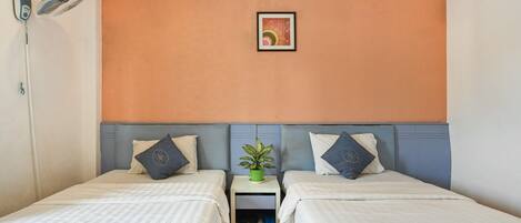 Una habitación de hotel con dos camas, una mesita de noche con una planta y un cuadro colgado en la pared.
