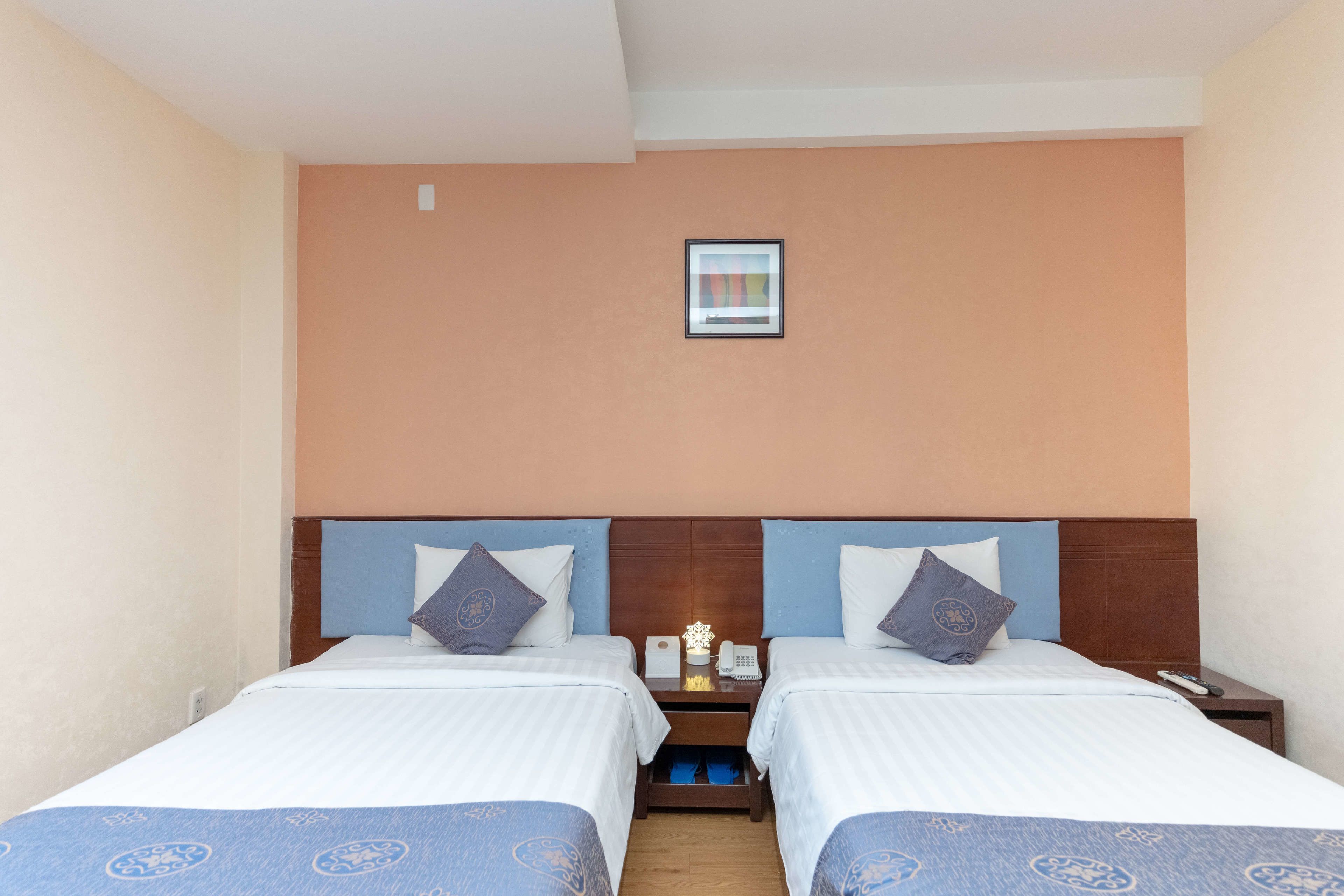 A hotel room with two beds, a nightstand with a phone and a lamp, and a small picture on the wall.