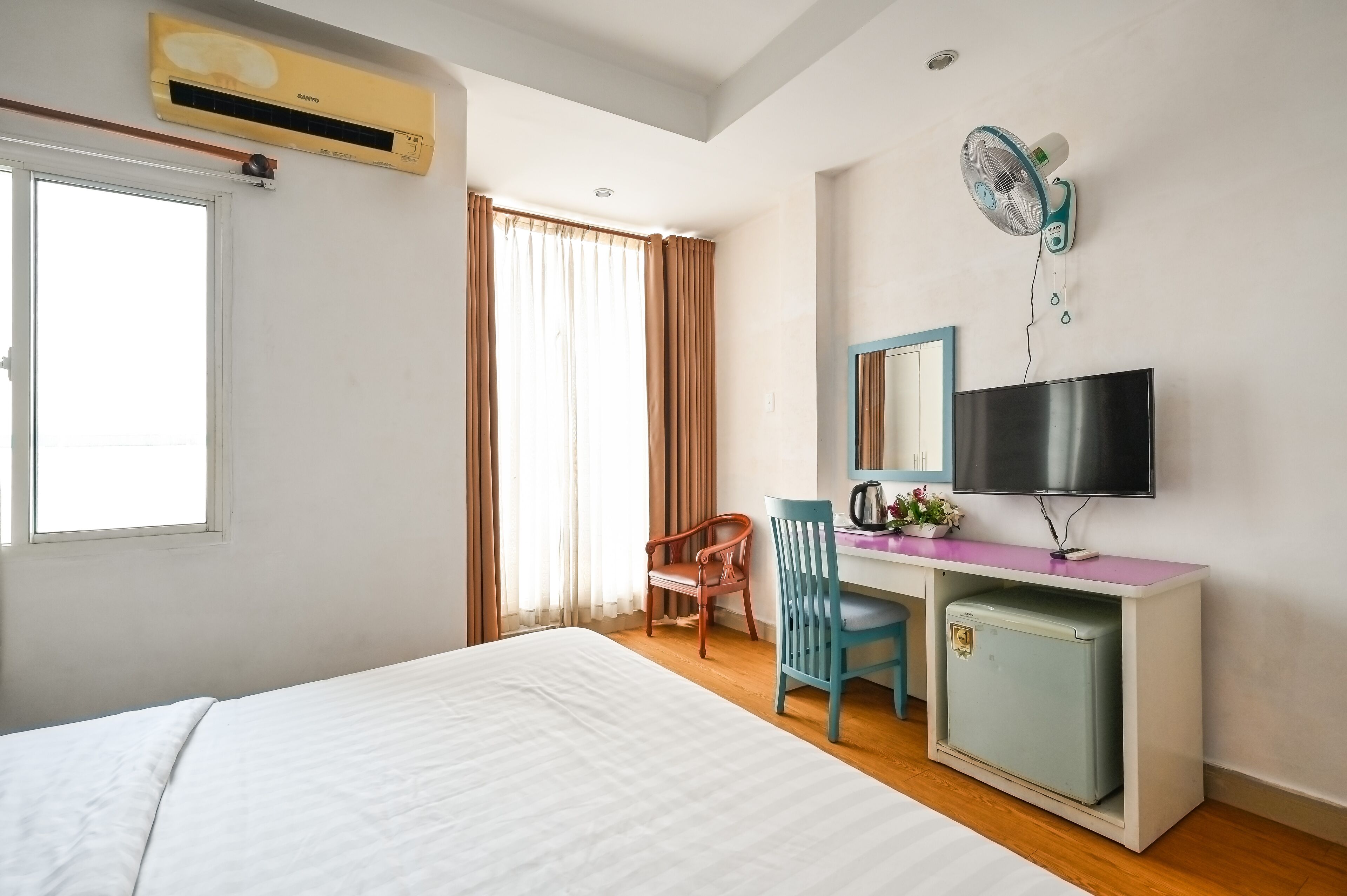 Une chambre d’hôtel avec un lit, un bureau avec une télévision, un petit réfrigérateur et une fenêtre avec des rideaux.