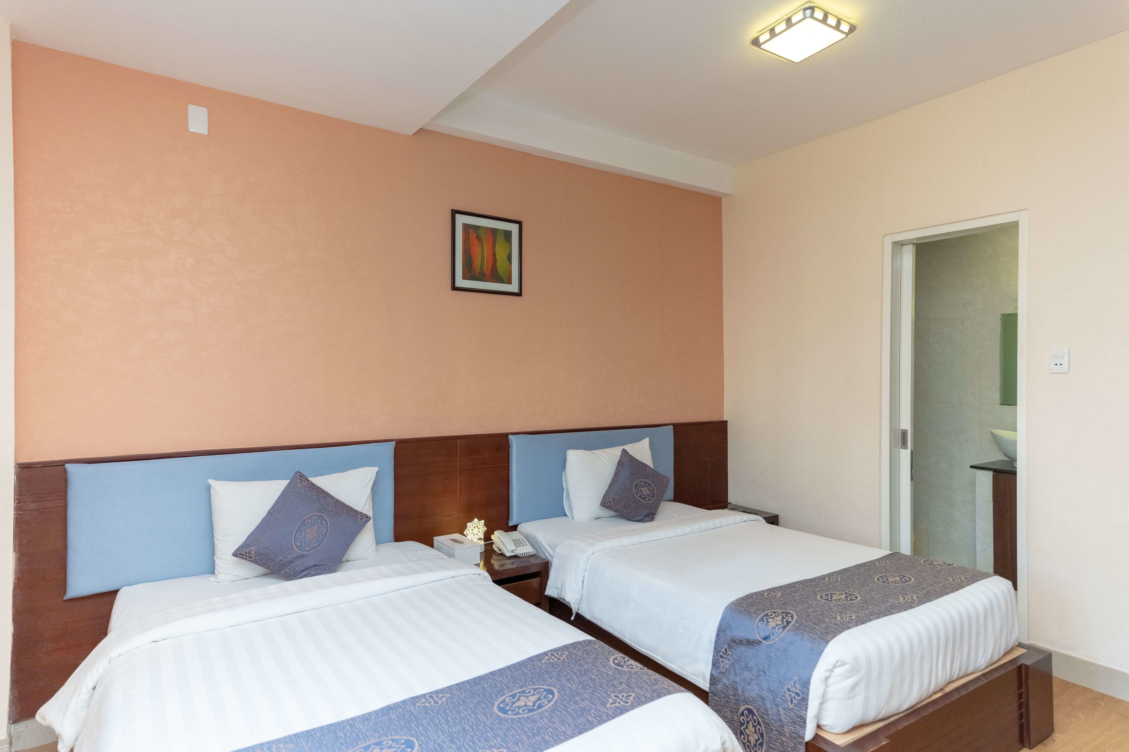 Habitación de hotel con dos camas, una mesita de noche, un teléfono fijo en la pared y una puerta que da al baño.