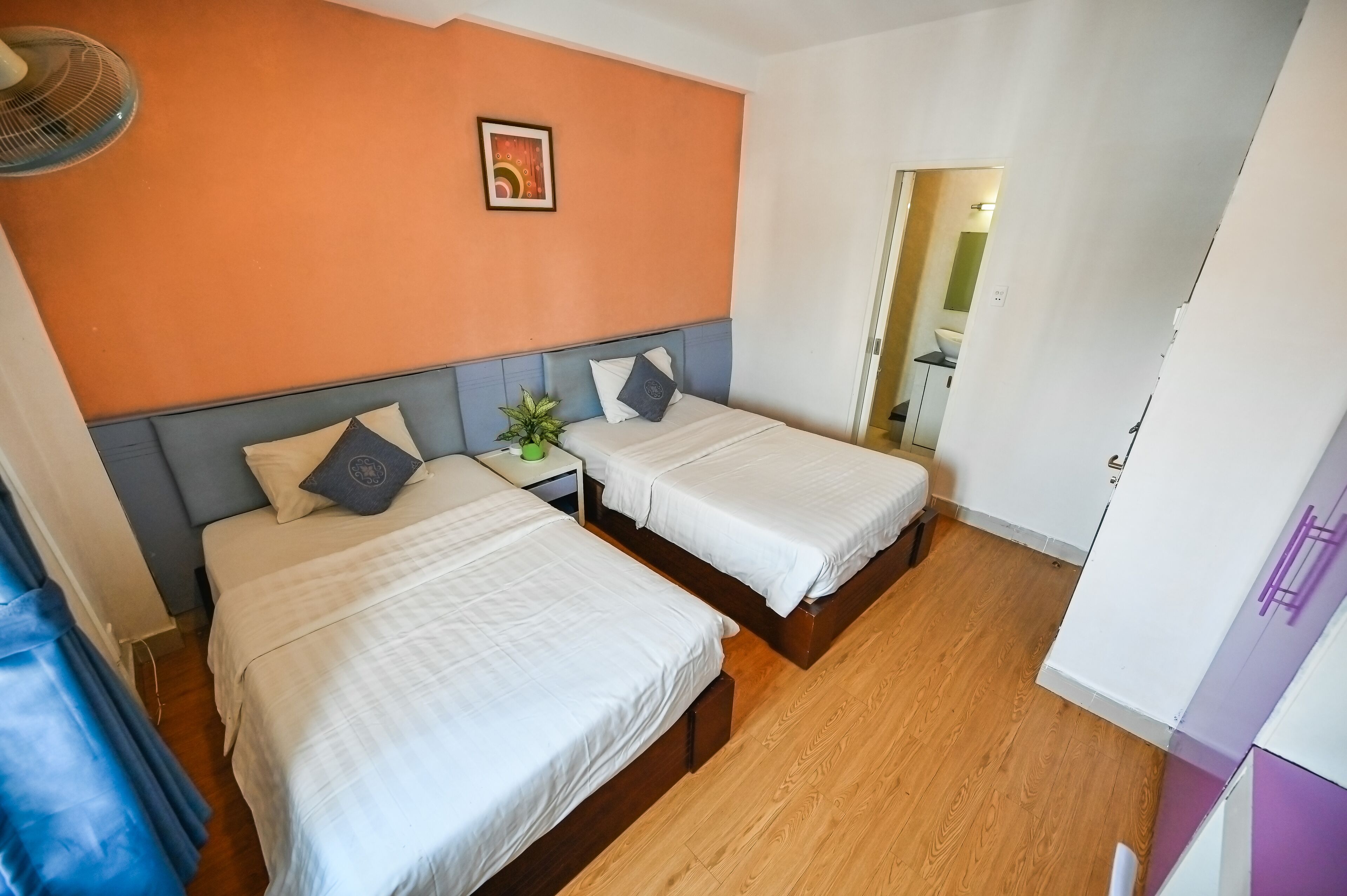 Habitación de hotel con dos camas, una mesita con una planta y un cuadro en la pared.