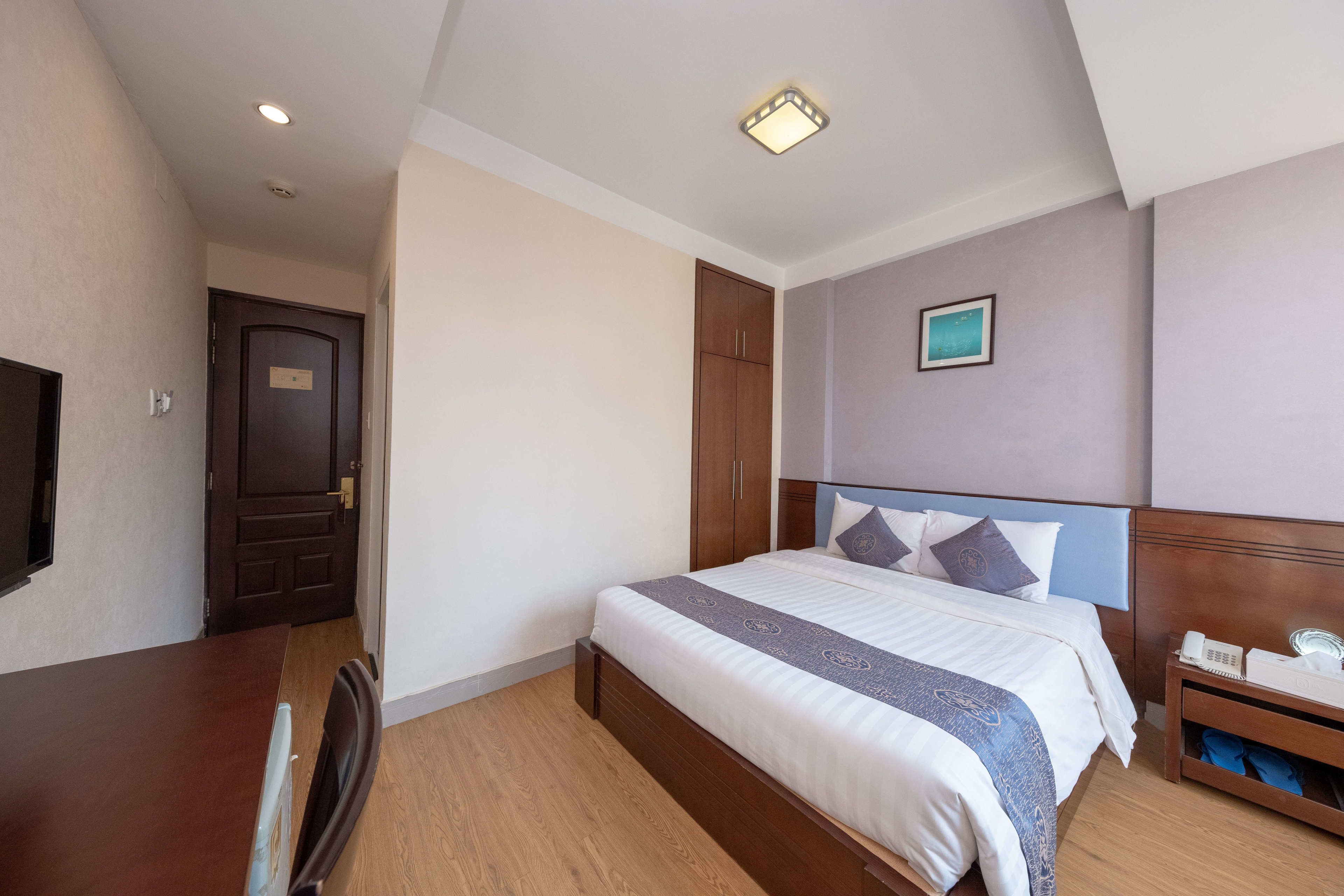 A hotel room with a bed, bedside table, and a desk.