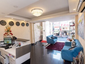 A hotel reception area with a desk, computer, phone, and decorative items. There are two blue armchairs and a red rug. - 99 Bui Vien Hotel (Ho Chi Minh City)
