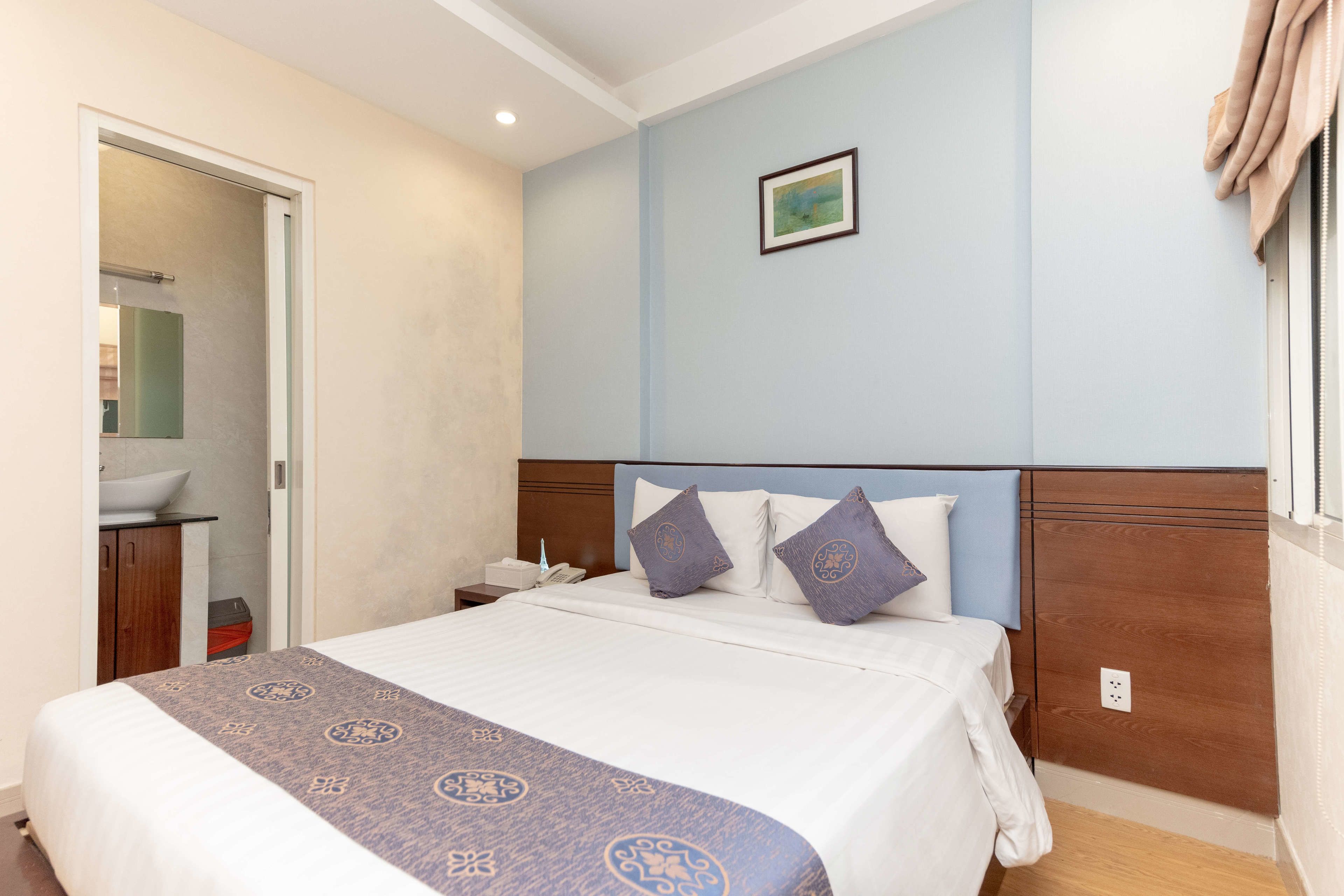A hotel room with a bed, a nightstand, a bathroom, and a window with curtains.
