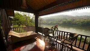 A wooden deck with a sofa and chairs overlooking a river and forested hills. - Nam Ou Riverside Hotel & Resort (Pak Ou)