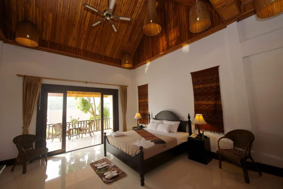 A spacious bedroom with a large bed, two bedside tables with lamps, a ceiling fan, and a balcony with a view.