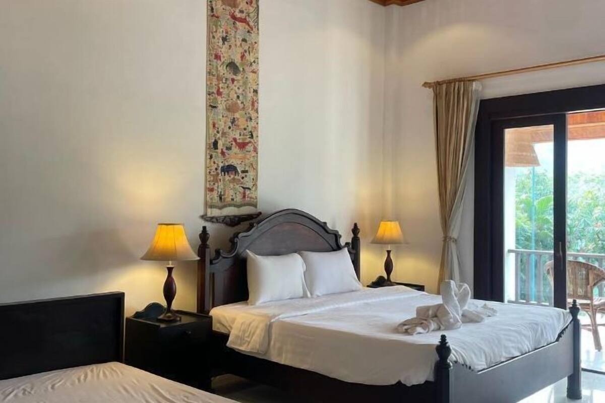 A hotel room with a bed, two bedside tables, a wall tapestry, and a balcony with a chair.