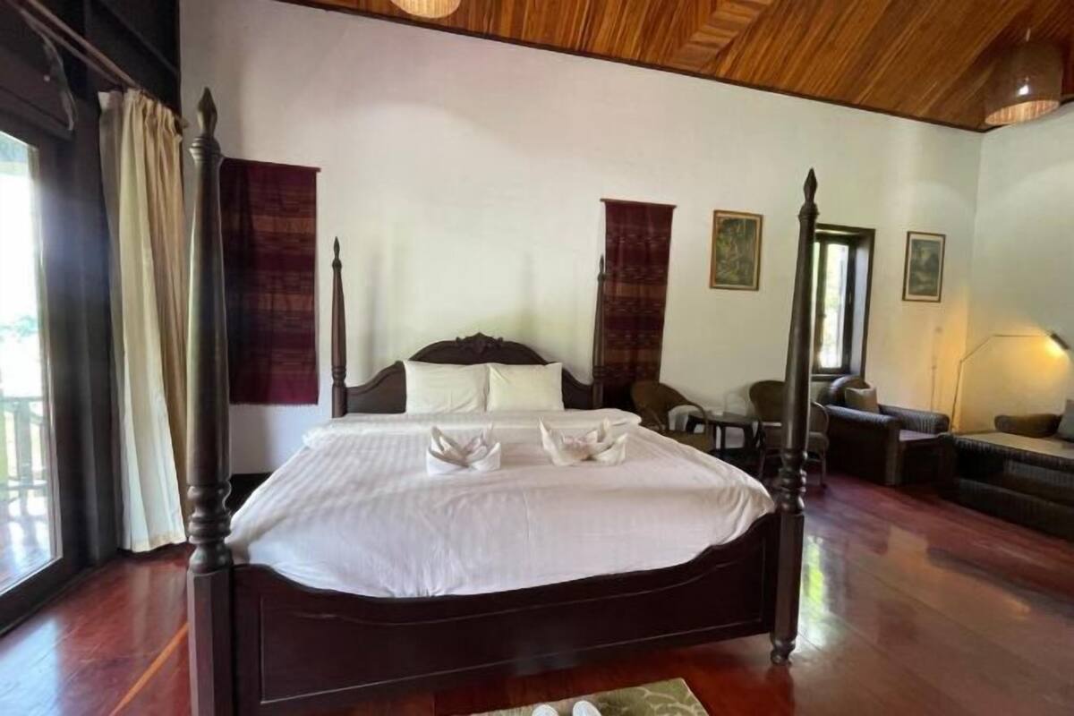 A large bed with a wooden frame, a sitting area with a sofa and chairs, and a dining table.