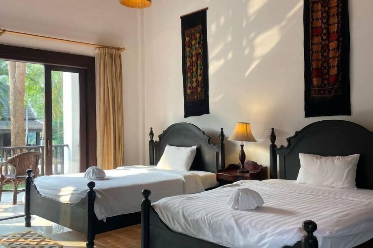 A hotel room with two beds, a balcony, and a view of greenery.