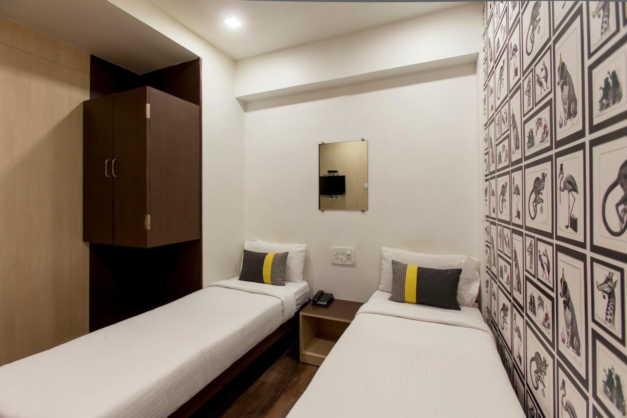 A hotel room with two single beds, a wardrobe, a mirror, and a wall with animal illustrations.