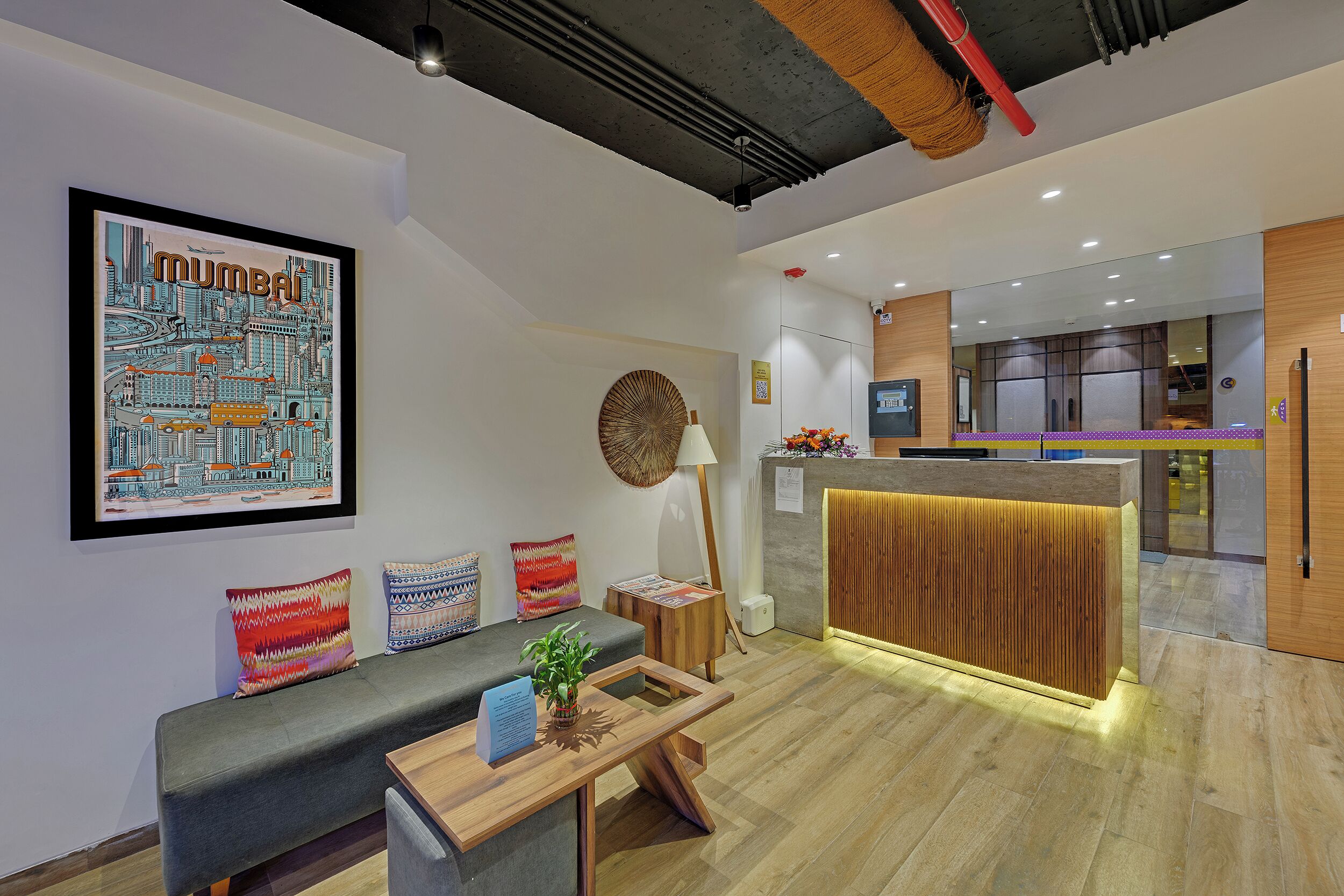 Un hall d’hôtel moderne avec un comptoir d’accueil, un espace salon et une grande œuvre d’art représentant un paysage urbain accrochée au mur.