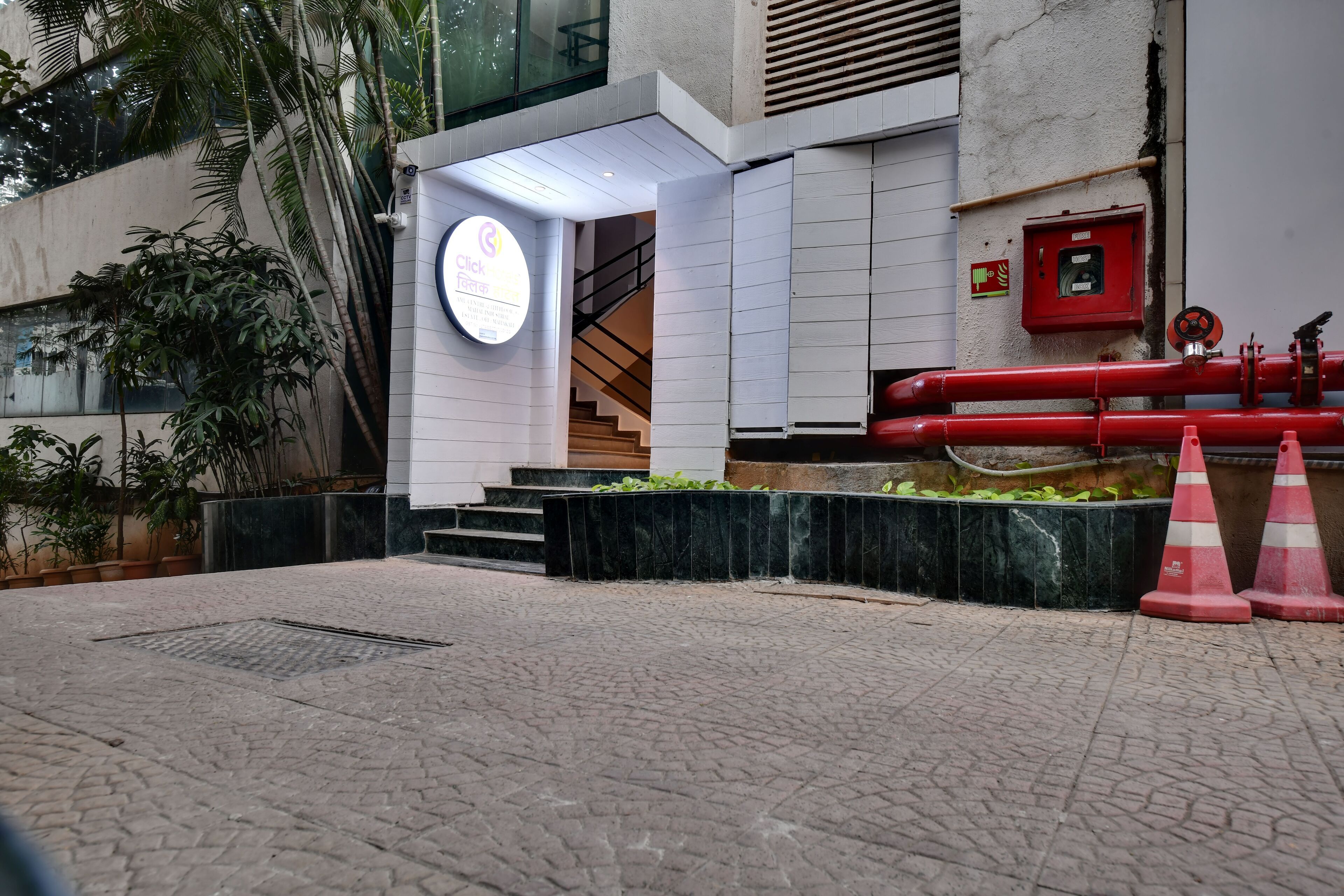 Entrada de un edificio con un letrero circular, una escalera y tuberías rojas.