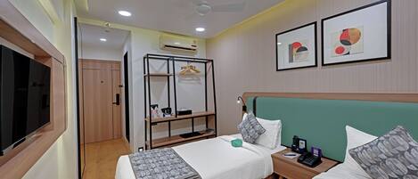 Ein Hotelzimmer mit zwei Betten, einem Fernseher, einem Kleiderschrank, einem Schreibtisch und einem Deckenventilator.