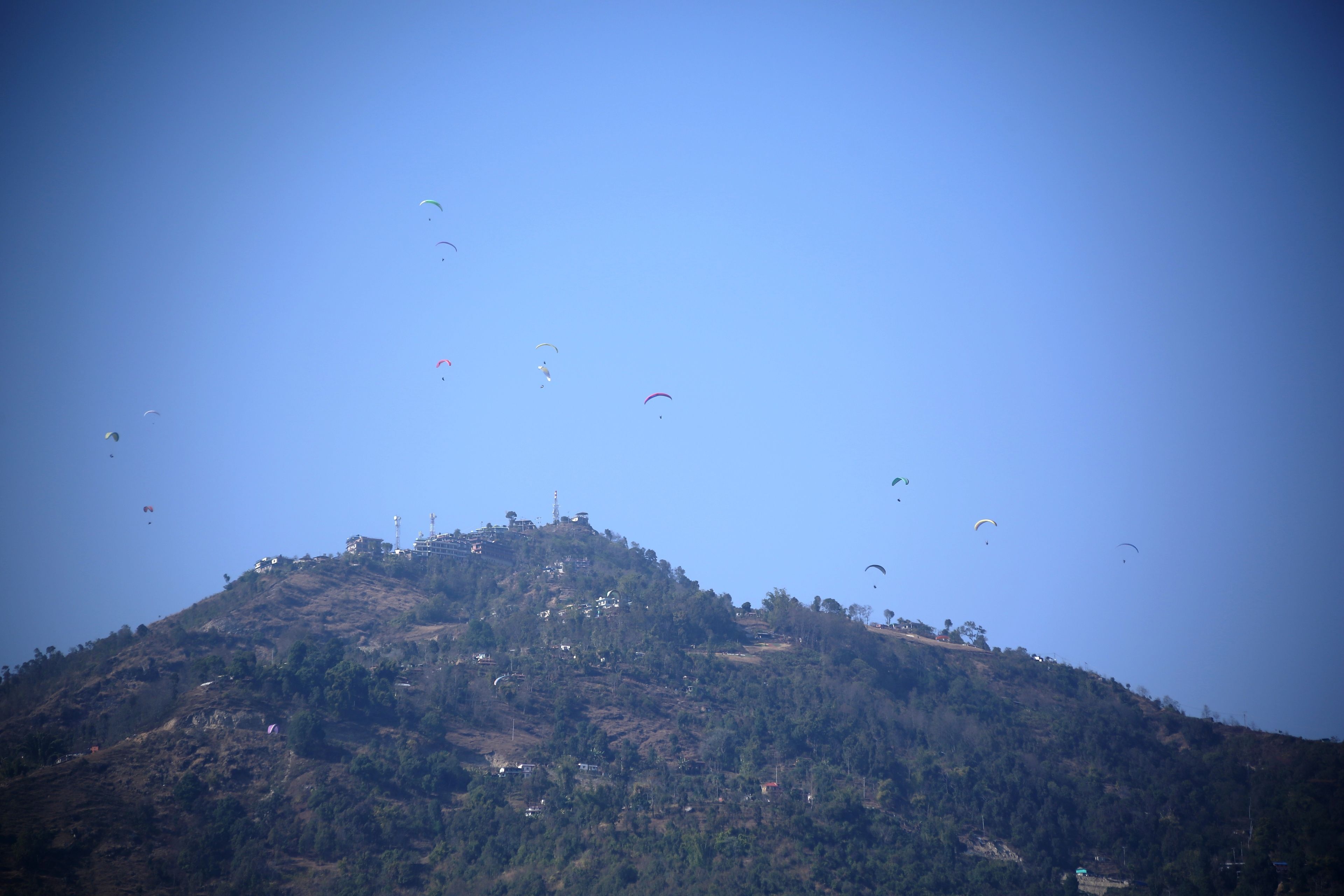 A hill with multiple kites flying in the sky.