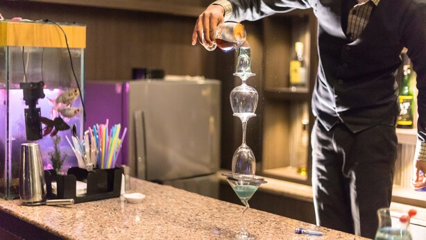 Un bartender vertiendo una bebida en una copa de martini.